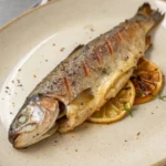 Savourez une truite au four parfumée au citron et aux herbes, simplement cuite avec du beurre et servie avec des légumes rôtis ou des pommes de terre.