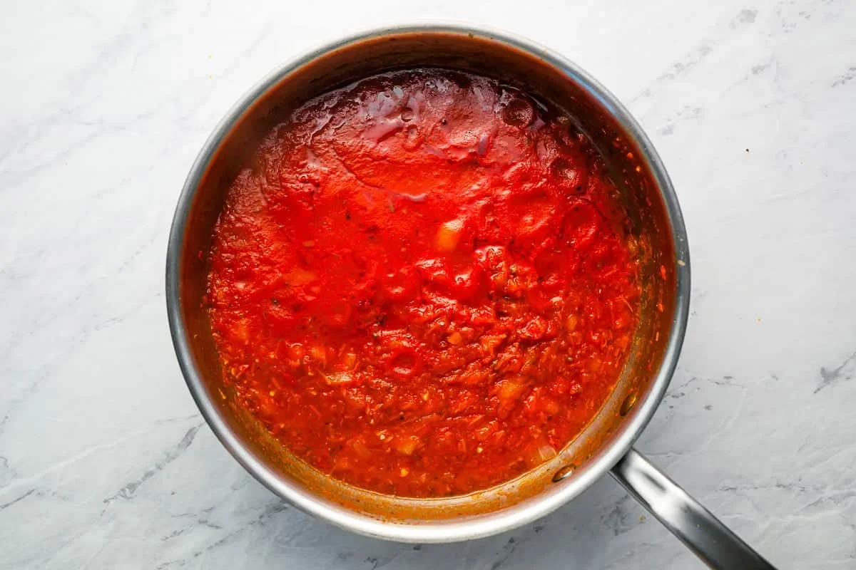 adding crushed tomatoes and seasonings to spaghetti sauce pot